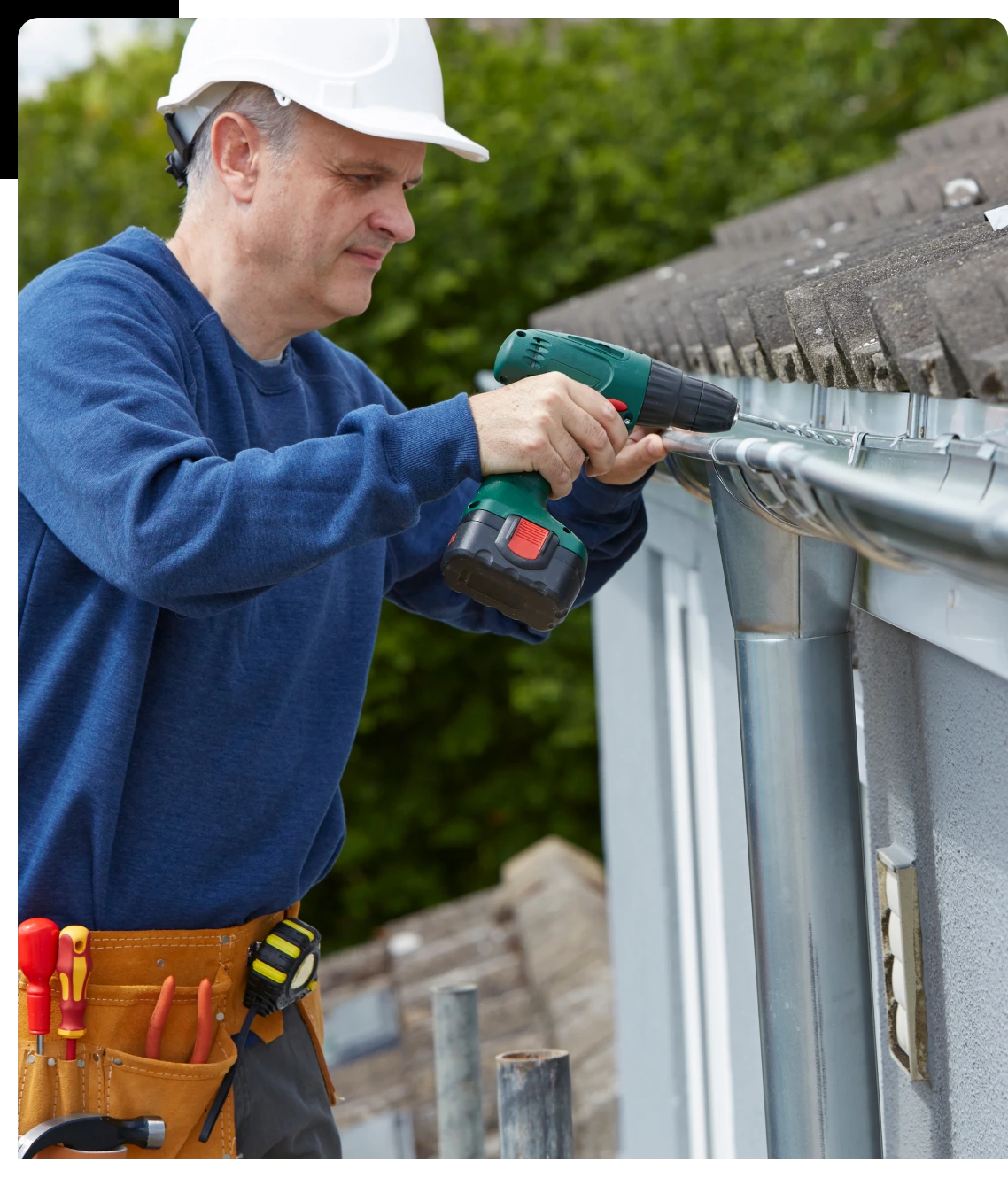 A man in blue shirt and hard hat working on gutter.